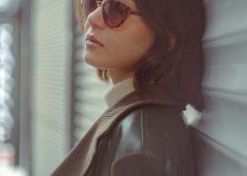 a woman wearing sunglasses leaning against a wall