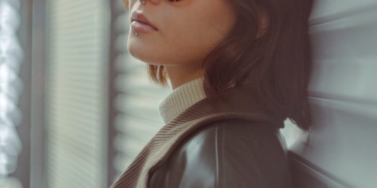 a woman wearing sunglasses leaning against a wall